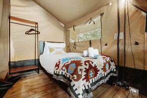 A tented room with a bed, a wooden bench, and a hanging clothes rack.