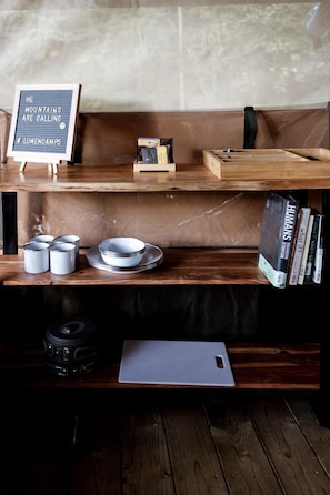 A wooden bench with a sign reading 'HE MOUNTAINS ARE CALLING #LUMENOAMPS' and a shelf with books and kitchenware.