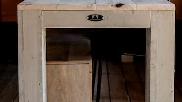 A wooden table with a drawer, set in a tent with a view of trees.