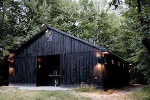 Un bâtiment de style rustique, ressemblant à une grange, avec une grande porte ouverte, un petit porche et une seule fenêtre sur le côté.