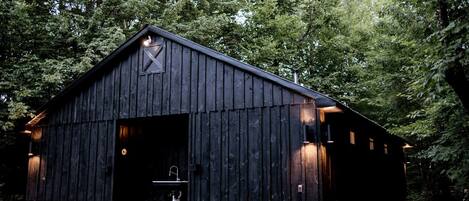 A rustic barn-style building with a large open door, a small porch, and a single window on the side.