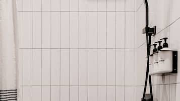 Une douche équipée d’un pommeau de douche à main, d’un robinet mural et d’un distributeur de savon.