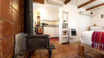 A cozy room with a wood-burning stove, a bed with a colorful blanket, and a kitchen area in the background.