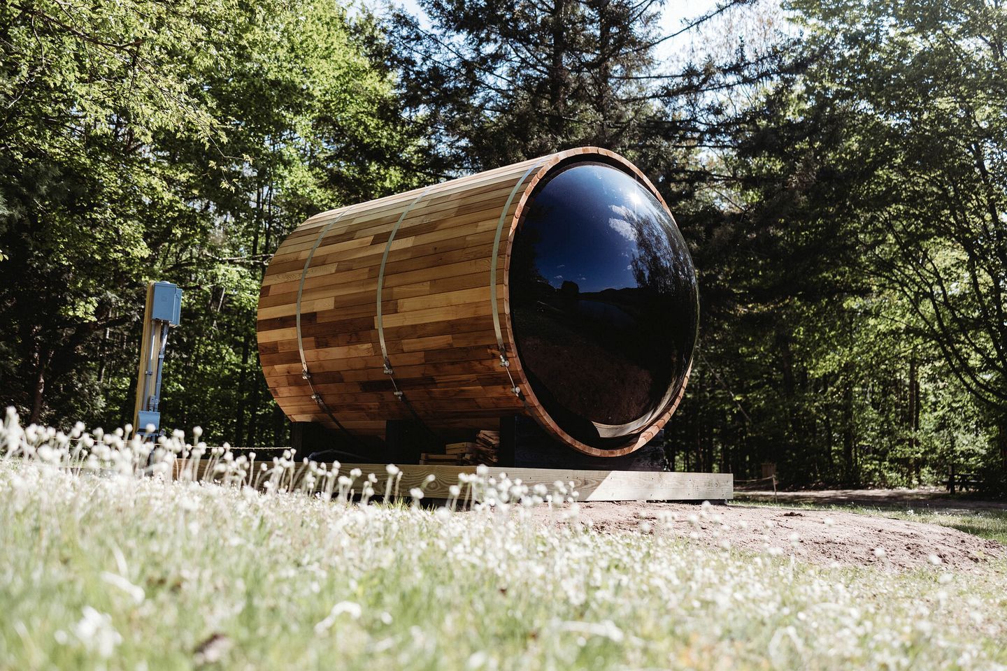 A large wooden barrel structure with a reflective surface, surrounded by a grassy area and trees.