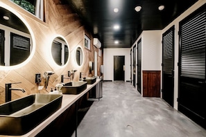 Un baño moderno con varios lavamanos, espejos redondos y una pared decorativa de madera.