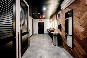 Pasillo con pared de madera, un cubo de basura, zona de lavamanos y letrero de salida.