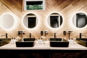 Un baño moderno con tres lavamanos, cada uno con un espejo redondo e iluminación integrada.