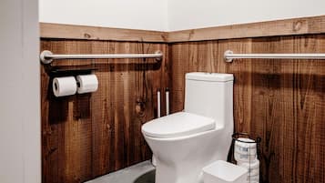A small, compact bathroom with a wooden wall, a white toilet, and two rolls of toilet paper on a rack.