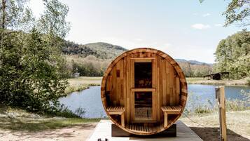 A wooden barrel-shaped structure with a bench inside, situated by a lake with a wooden deck in front.