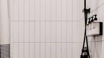 A shower with a handheld showerhead, a wall-mounted faucet, and a soap dispenser.