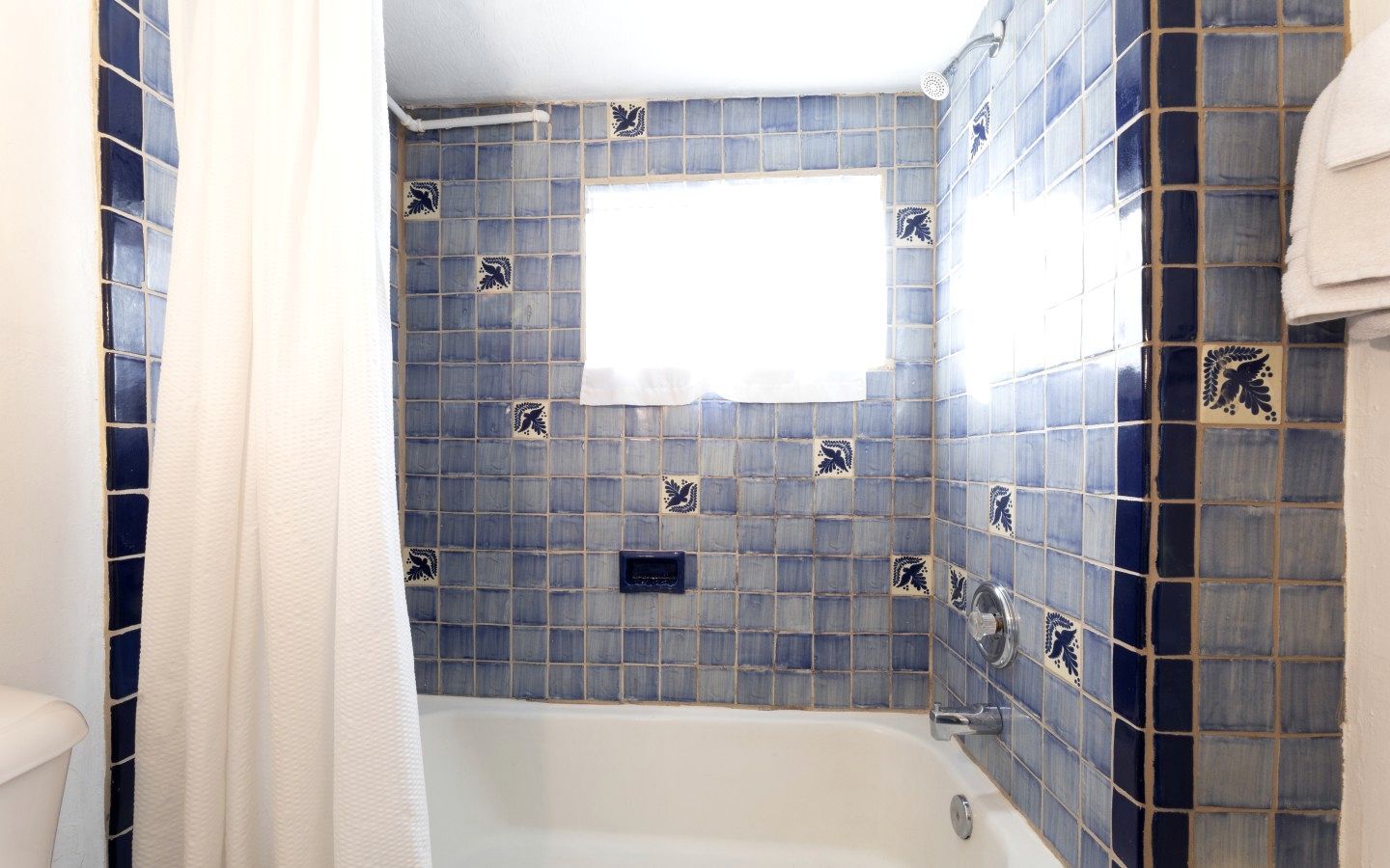 A bathroom with a bathtub, blue tiled walls, and a window.
