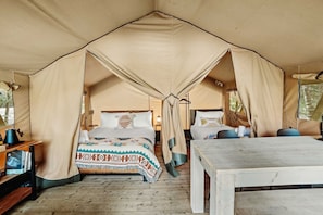 Eine Zeltunterkunft mit Bett, Nachttisch und einer kleinen Schreibtischzeile.