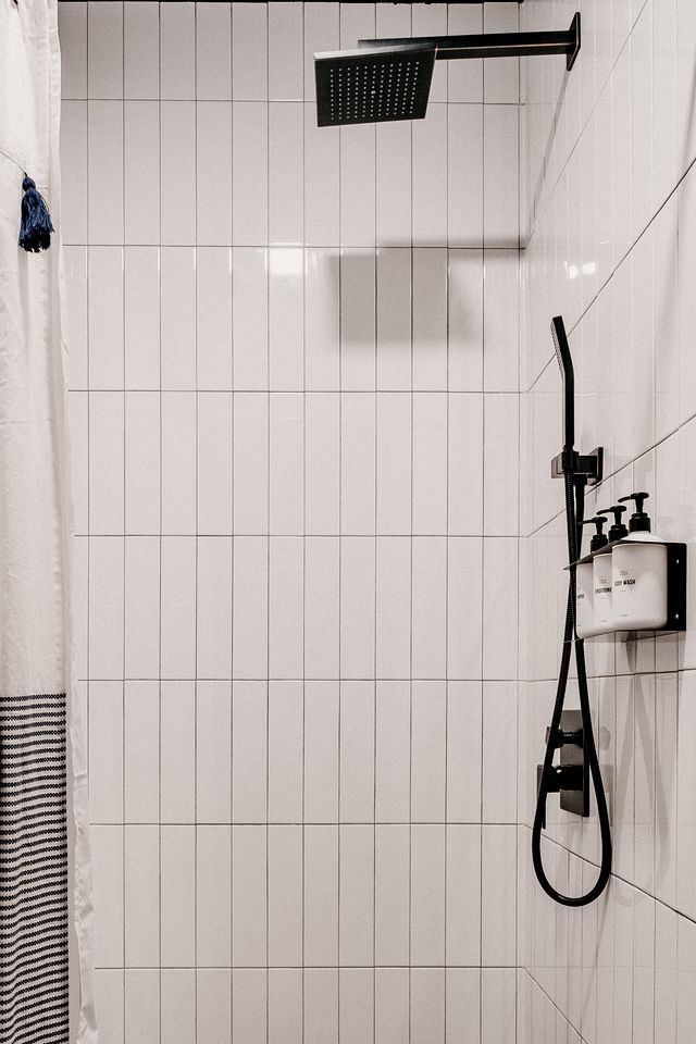 En dusch med ett duschhuvud som kan hållas i handen, en väggmonterad blandare och en tvåldispenser.