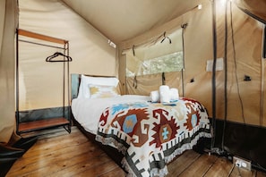 A tented room with a bed, a wooden bench, and a hanging clothes rack. - Charming Safari Tent with Sauna and Fire Pit in North Woodstock, New Hampshire (North Woodstock)