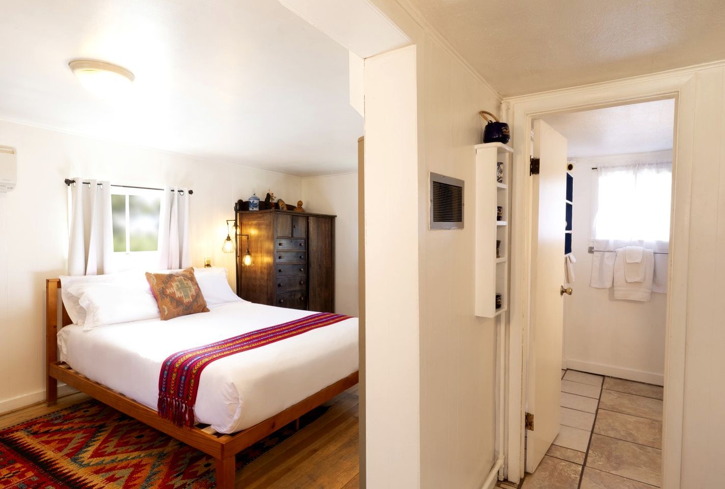 A bedroom with a bed, a wardrobe, a door leading to a bathroom, and a patterned rug.