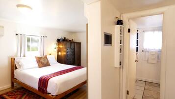 A bedroom with a bed, a wardrobe, a door leading to a bathroom, and a patterned rug.