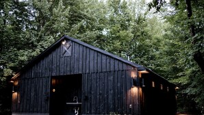 A rustic barn-style building with a large open door, a small porch, and a single window on the side.