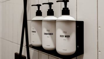 Ein schwarzes Regal mit drei weißen Flaschen, beschriftet mit 'Shampoo', 'Conditioner' und 'Body Wash', an einer weiß gefliesten Wand befestigt.