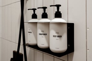 Ein schwarzes Regal mit drei weißen Flaschen, beschriftet mit 'Shampoo', 'Conditioner' und 'Body Wash', an einer weiß gefliesten Wand befestigt.