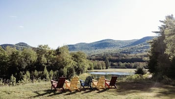 Three Adirondack chairs facing a lake with mountains in the background.