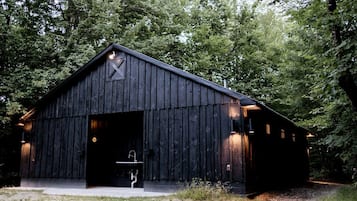 En rustik byggnad i stil med ett gammalt ladugård, med en stor, öppen dörr, en liten veranda och ett enda fönster på sidan.