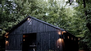 Un bâtiment de style rustique, ressemblant à une grange, avec une grande porte ouverte, un petit porche et une seule fenêtre sur le côté.