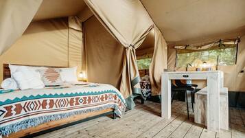 A tented room with a bed, a small table, and a window.