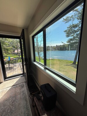 A room with a large window overlooking a lake, a patio with outdoor furniture, and a black suitcase on the floor. - Newly renovated 3-bedroom lake home in Gwinn, Michigan - check for availability  (Gwinn)