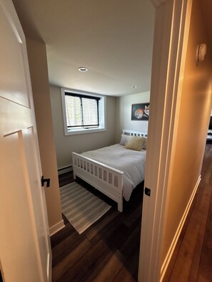 A bedroom with a white bed, a window with blinds, a rug, and a painting on the wall. - Newly renovated 3-bedroom lake home in Gwinn, Michigan - check for availability  (Gwinn)