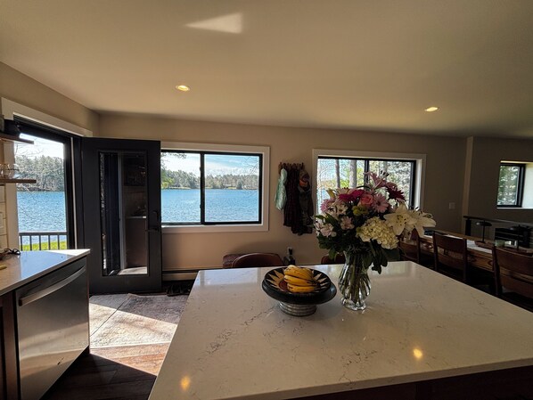 A kitchen with a large island, a view of a lake, and a vase with flowers.
