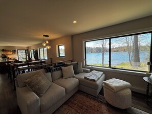 A modern living room with a large window overlooking a lake, a cozy seating area, and a dining space. - Newly renovated 3-bedroom lake home in Gwinn, Michigan - check for availability  (Gwinn)