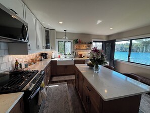 A modern kitchen with a large island, a stove, and a view of a lake through the windows.