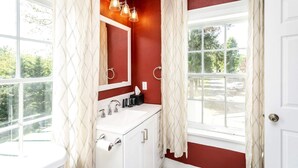 Un bagno con un mobile lavabo bianco, uno specchio, un porta asciugamani e una finestra con tende.