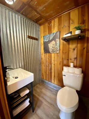 Une salle de bain avec un lavabo blanc, des toilettes et un mur en bois.