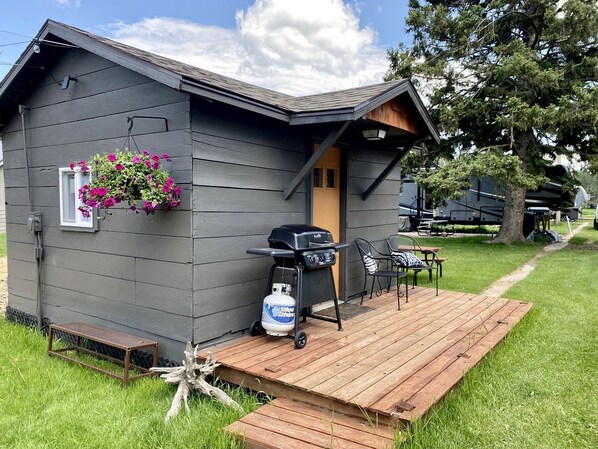 A small cabin with a deck, a barbecue grill, and outdoor seating.