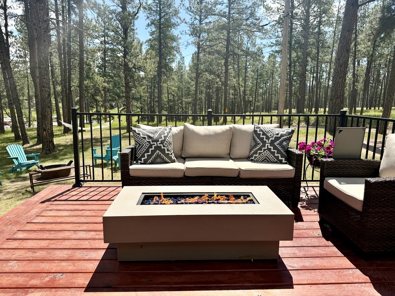 A deck with a sofa and a fire feature, surrounded by chairs and a railing.