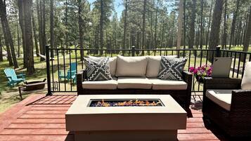 A deck with a sofa and a fire feature, surrounded by chairs and a railing.