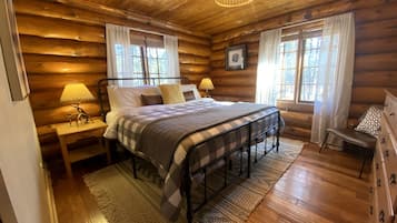 Un dormitorio de cabaña de madera con cama, mesitas de noche, cómoda y lámpara de araña.