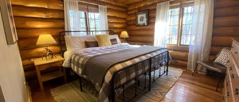 Ein Schlafzimmer einer Holzhütte mit einem Bett, Nachttischen, einer Kommode und einem Kronleuchter.