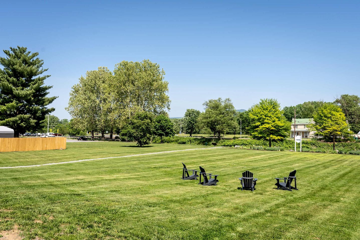 A grassy outdoor area with several Adirondack chairs and a wooden fence.