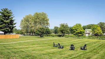 A grassy outdoor area with several Adirondack chairs and a wooden fence.