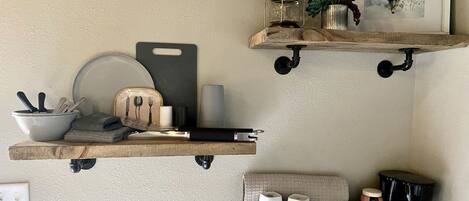 A kitchen with wooden shelves holding kitchenware, a coffee maker, and a framed picture.