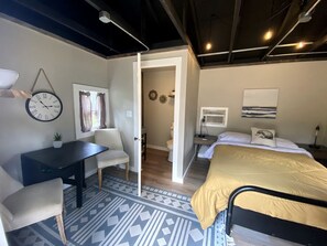 A room with a bed, a desk, a chair, a clock, and a door leading to another room. - Tiny Cabin with Beautiful Lake Views in Rapid City, South Dakota (Rapid City)