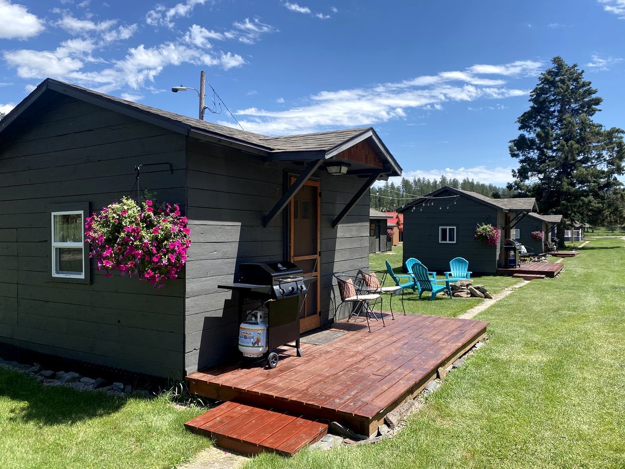 A small cabin with a deck, a grill, and outdoor seating.