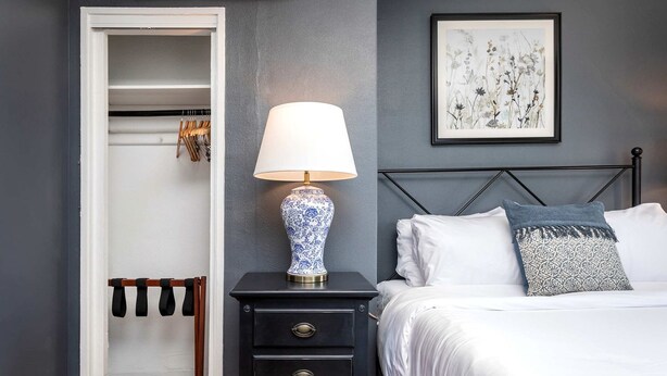 Un dormitorio con cama, una mesita de noche con lámpara, un armario y un cuadro en la pared.