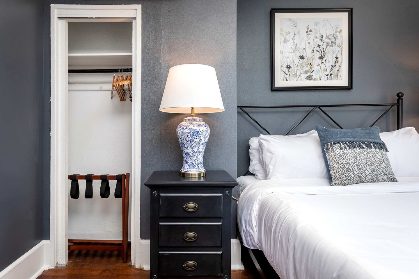 A bedroom with a bed, a bedside table with a lamp, a wardrobe, and a framed picture on the wall.