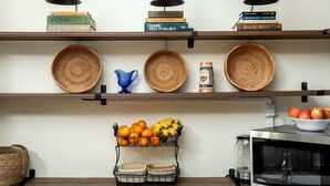 Una cocina con estantes que contienen libros, cestas tejidas y un frutero.