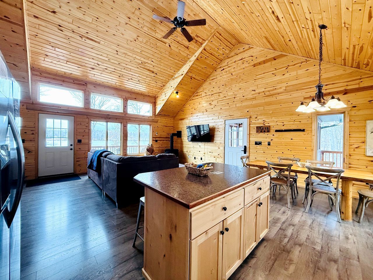 A log cabin interior with a kitchen, dining area, and living room, featuring wooden walls and floors.