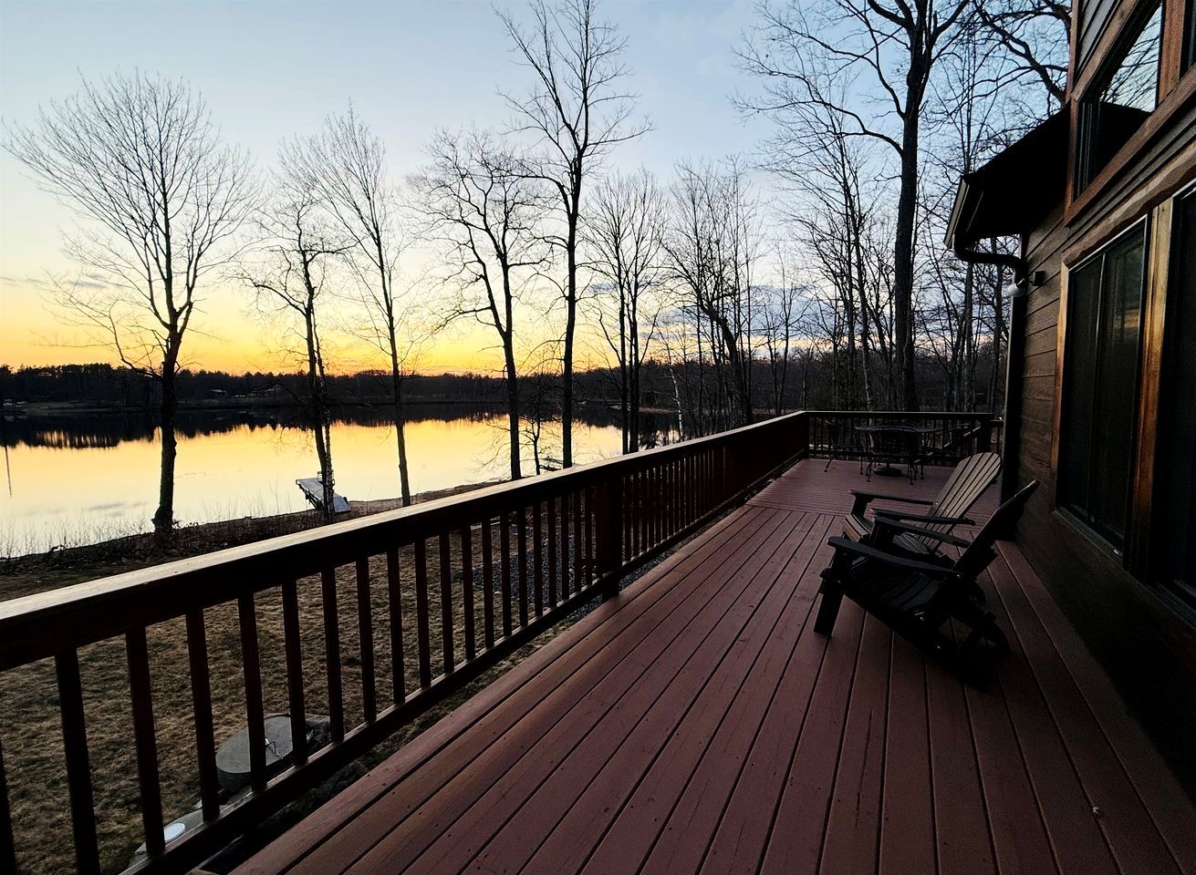 A wooden deck with chairs, a railing, and a view of a lake and trees.