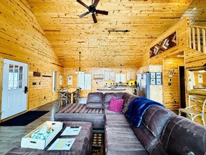 A log cabin interior with a sofa, a dining table, and a kitchen area.